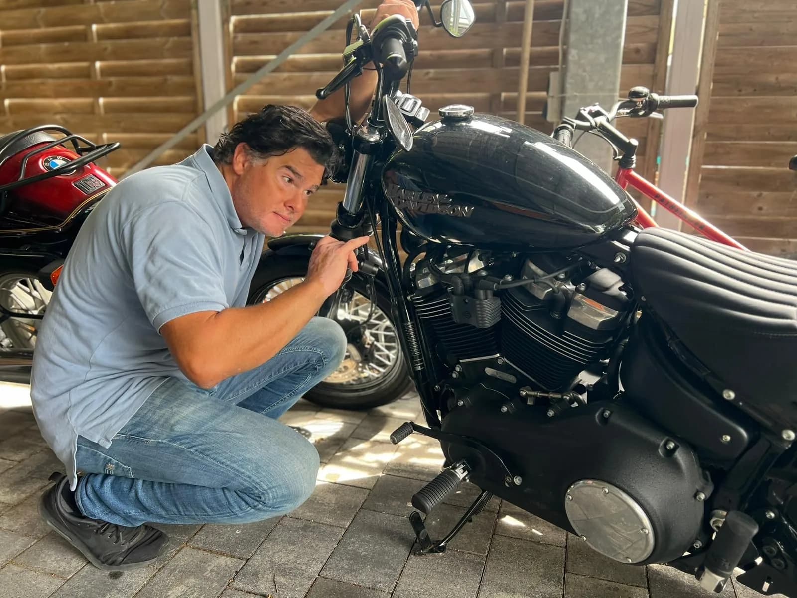 Ferdinand Wolf kniet neben einem schwarzen Motorrad und misst am Tank