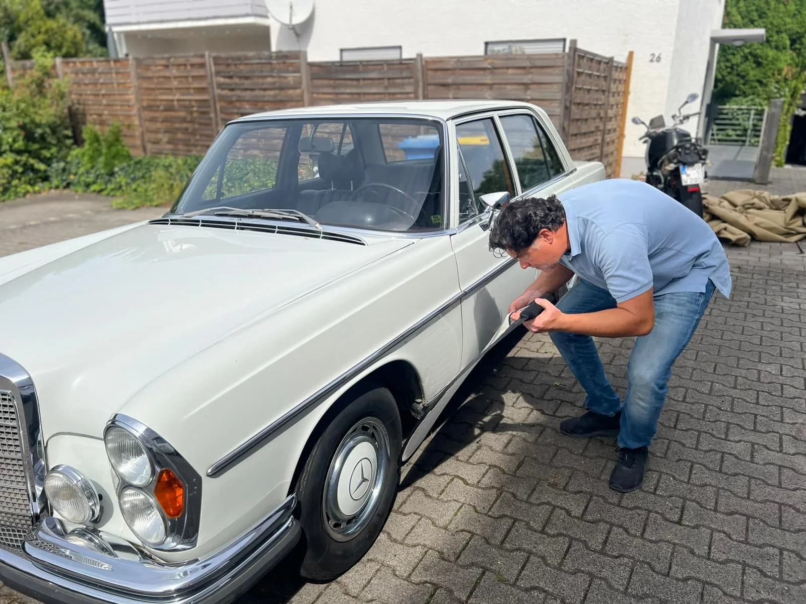Ferdinand Wolf prüft die Seite einer weißen Mercedes-Limousine mit einem Messgerät