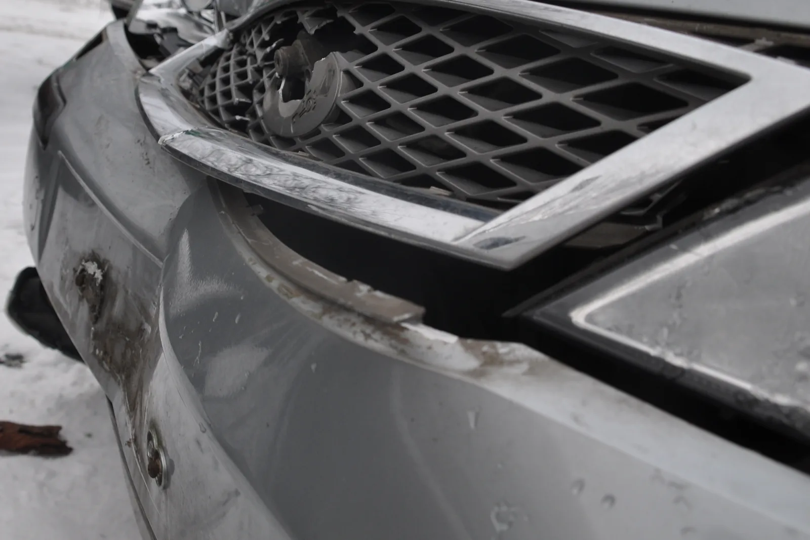 Zerstörter Kühlergrill mit herausgerissenem Emblem an einem Fahrzeug im Schnee