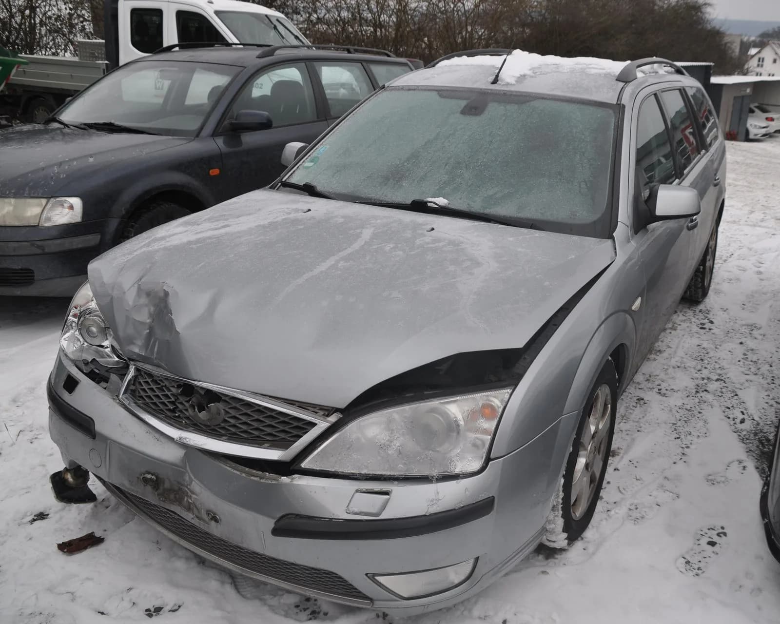 Silberner Kombi mit eingedrückter Front, Teile liegen im Schnee