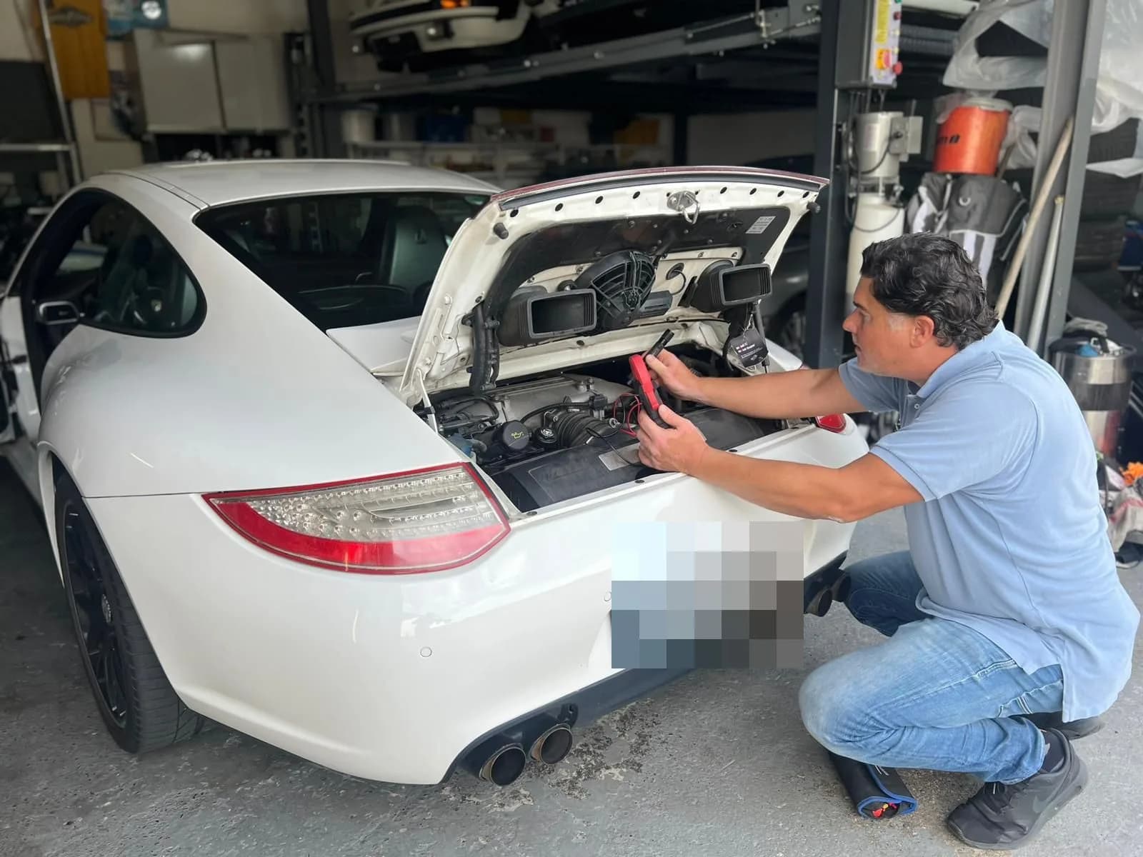 Kfz-Sachverständiger prüft mit einem Messgerät den geöffneten Heckraum eines weißen Sportwagens