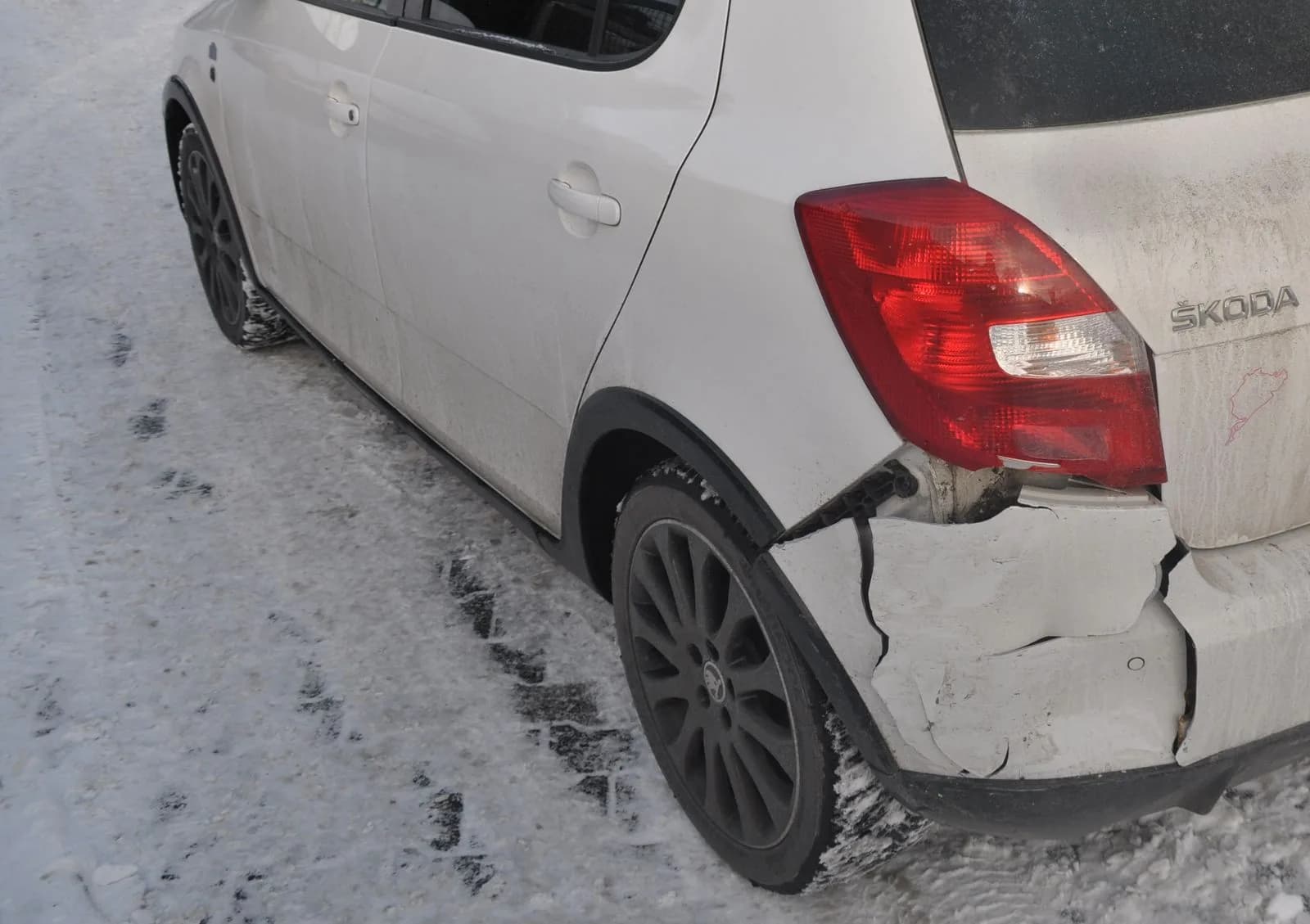Weißer Kleinwagen im Schnee mit aufgerissenem Heckstoßfänger