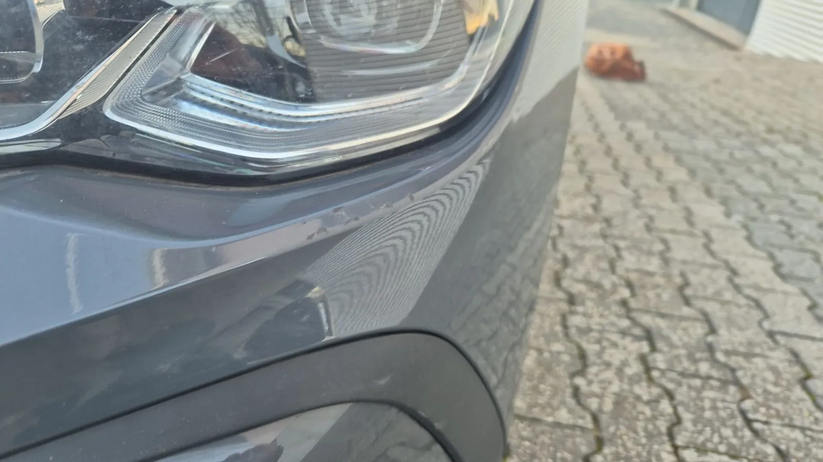 Lackabplatzer und Schrammen am Frontstoßfänger unter dem Scheinwerfer